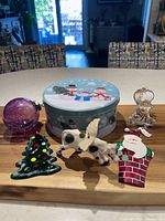 All six items displayed on board: purple crackle ball, fused glass tree, crystal bear, tin Santa, flying cow, snowman cookie tin
