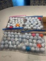 Five zipper bags filled with approximately 100 assorted golf balls on countertop
