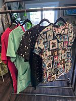 Rack holding assorted scrub garments: visible mint green, dark gray/magenta, black cat print and multicolour dog/cat patchwork tops