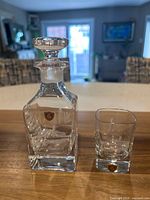 Decanter with stopper beside shot glass, etched ship visible, labels present