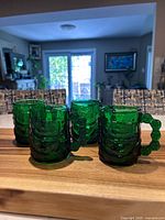 Four emerald green Arcoroc snowman mugs on wooden surface