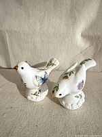 Front view of both porcelain bird shakers showing floral and butterfly motifs