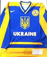 Full front view of blue/yellow Ukraine hockey jersey showing crest, wordmark, federation patch, autograph at bottom