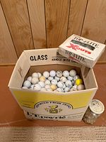 Box of loose assorted golf balls, jar of tees visible