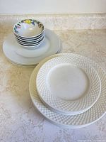Stacked bowls on plain plates beside stack of textured-rim plates