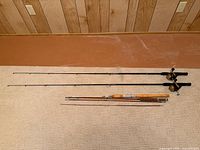 Overall view of two black fiberglass rod-reel combos and two vintage wood rods laid out