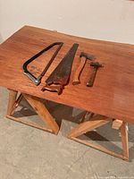 Sawhorses with tools displayed on top: hacksaw, panel saw, hatchet, hammer
