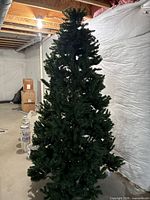 Full view of assembled green artificial Christmas tree standing in unfinished basement