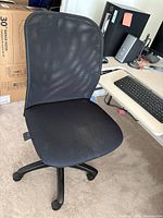 Three-quarter front view of black mesh back office chair showing seat, backrest, base and casters