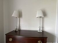 Pair of clear crystal table lamps with pleated white shades on dresser