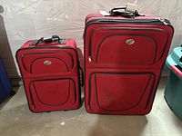 Front view of both red American Tourister suitcases showing size difference, exterior pockets, telescoping handles retracted