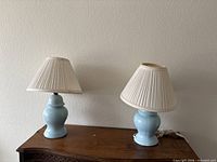 Two matching light blue ceramic lamps with cream pleated shades on wooden surface