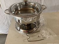assembled stainless steel chafer with glass lid, stand and lid rest, partially wrapped in original plastic