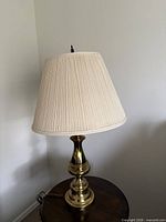 full view of brass table lamp with pleated cream shade on side table