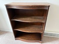Full view of bookcase showing three shelves, carved trim, wear