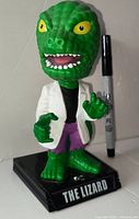 Front view of The Lizard bobble-head on base with Sharpie for scale