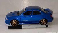 Side view of blue Subaru WRX diecast with marker for scale