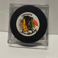 Front view of Chicago Blackhawks puck with visible Chris Chelios signature inside clear display case