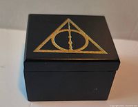 Closed black music box top view showing gold Deathly Hallows symbol