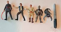 All five Star Wars action figures lined up beside marker for scale