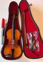 Open case showing miniature violin, two bows, micro violin packet and scale marker