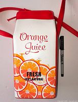 Front view of orange juice carton shoulder bag next to Sharpie for scale