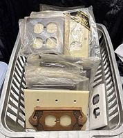 Basket containing assorted brown and ivory plastic outlet and switch plates, some sealed