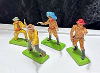 Front view of four painted metal cowboy figures on green bases