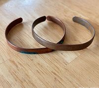 Pair of copper cuff bracelets on wooden surface