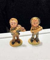 Front view of both child musician figurines showing instruments and paint