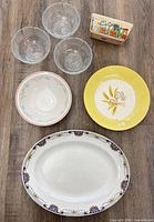 Top-down view showing entire lot of platter, yellow plate, white bowl, three glass bowls and napkin holder