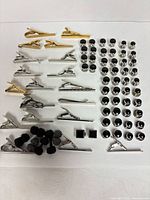 Overview of tie clips, shirt studs, cufflinks and silk knots laid out in rows