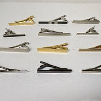 Nine tie bar clips laid out showing varied finishes