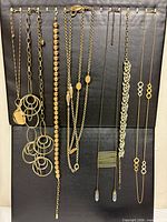 All nine gold-tone necklaces displayed on black board