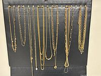 Full view of fourteen gold-tone necklaces hanging vertically