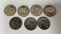 Obverse view of seven of the eight Kennedy half dollars showing dates and circulation wear