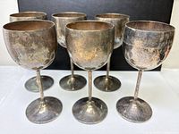 Front view of six tarnished silver-plated brass goblets