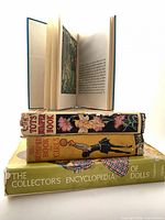Stacked view of three books showing spines: The Tots Bumper Book, The Bumper Book for Girls, The Collector's Encyclopedia of Dolls; top book open to illustrated page