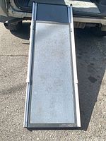 Ramp fully extended on ground behind vehicle, showing grey non-slip surface and silver aluminum rails