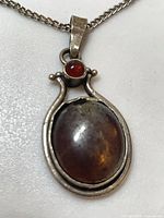 Full view of pendant and part of chain showing oval dichroic glass cabochon and red accent cabochon in sterling setting