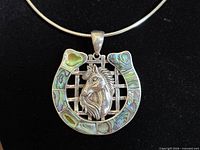 Front view of sterling silver horseshoe pendant with horse head and shell inlay on torque chain