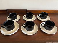 Six black cups on white saucers arranged on wooden surface
