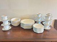 Full set of stacked white octagonal plates, bowls, cups and saucers on table
