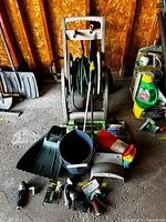 Wide view of entire lot showing hose reel cart, hose, bucket, dustpans, packaged nozzles, cloths, mitt, sprinkler