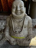 Front view of grey hollow Buddha statue with bead necklace