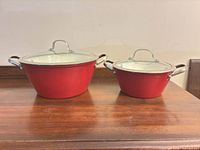 Two red enameled cast iron pots with glass lids side by side