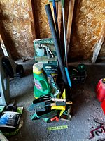 Lot overview showing fertilizer jug, boxed sprayer, long-handled tools, tote with hand tools