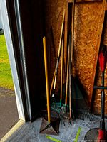 Group of long-handled garden tools leaning against wall