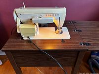 Singer sewing machine mounted in wooden cabinet, side view with power cord visible