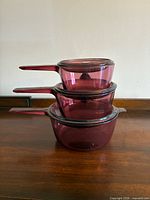 Three stacked cranberry glass saucepans showing relative sizes